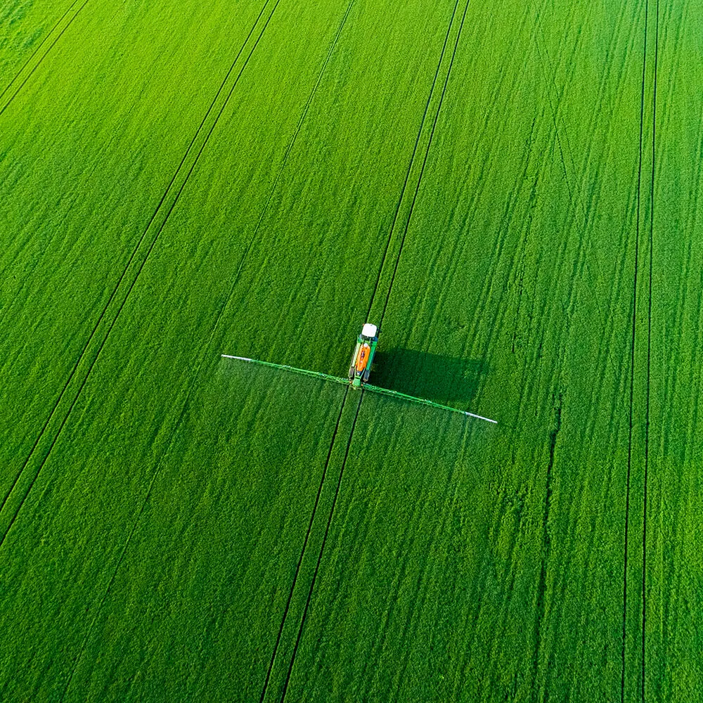 Aerial view of a tractor spraying a green field